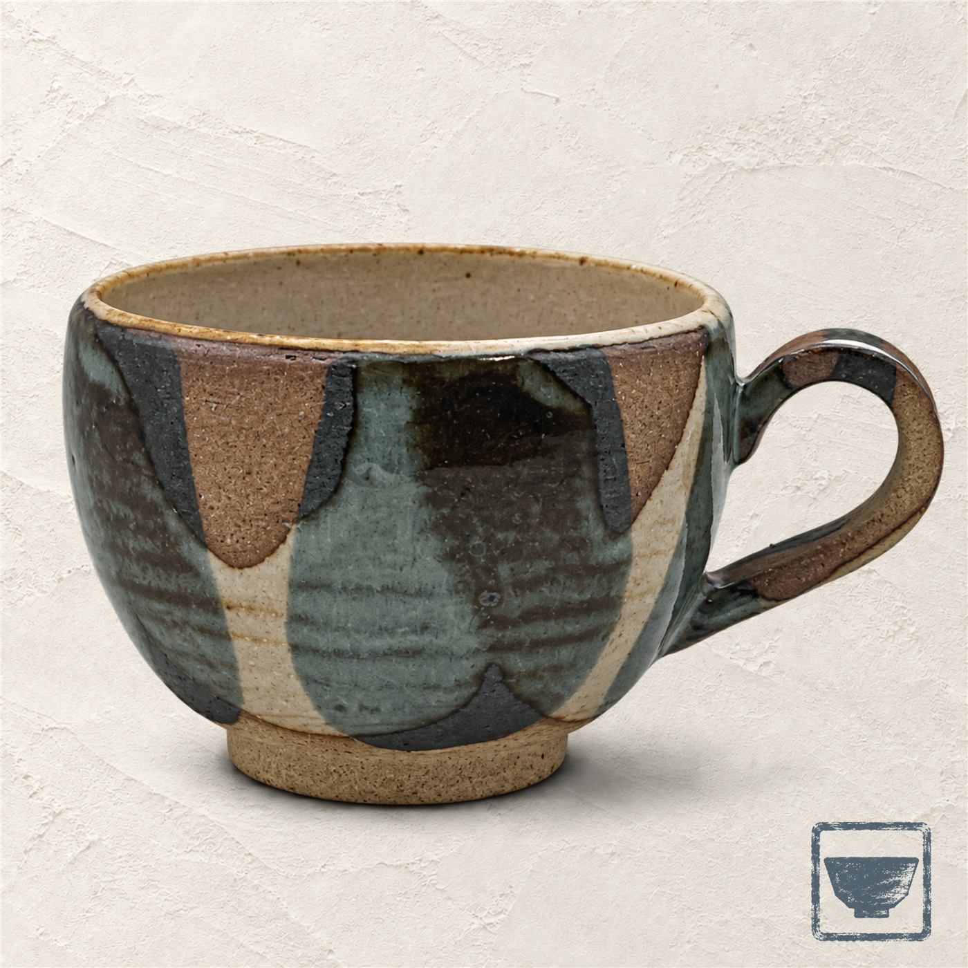A stoneware mug in earth and indigo glazes on ivory plaster, an indigo brush stroke behind the handle